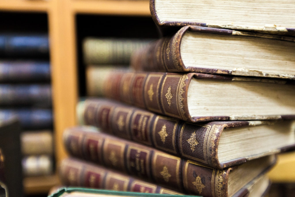 Stos starych, bogato zdobionych książek w skórzanych oprawach na tle bibliotecznych regałów, symbolizujący klasyczną literaturę i ukryte znaczenia.